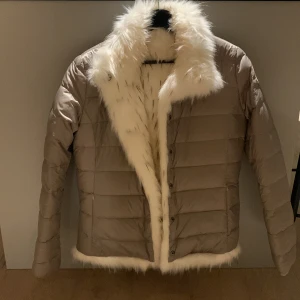 Beige pufferjacka med päls från Colmar - Säljer en beige pufferjacka från Colmar med fluffig vit fuskpäls på krage och insida. Jackan har quiltad design, långa ärmar och knappar framtill. Märkeslogga på ärmen och coola detaljer som gör den extra snygg. Perfekt för dig som vill sticka ut i vinter. Man kan vända den ut och in för en annan look. Beroende på vad man själv föredrar. Finns inga defekter på jackan och den är som ny. Pris kan såklart diskuteras 🚚♻️