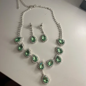 Grönt glittrande halsband & örhängen - Set med halsband och örhängen med stora droppformade gröna stenar omgivna av gnistrande små stenar. Silverfärgad kedja och infattning, perfekt för att sticka ut. Stenarna har en riktigt snygg glittrig effekt och ger en lyxig känsla.