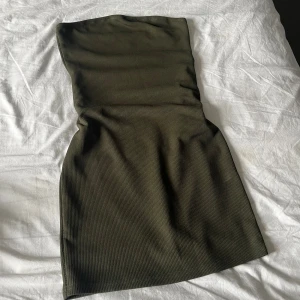Mörkgrön ribbad tubklänning - Säljer en mörkgrön tubklänning med ribbad struktur. Klänningen är kort och har en tight passform som framhäver figuren. Perfekt för dig som gillar minimalistisk stil och vill ha något enkelt men snyggt. Materialet är mjukt och stretchigt för extra komfort.