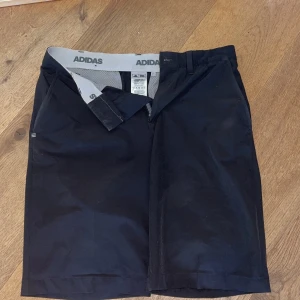 Svarta shorts från Adidas, storlek 30 - Snygga svarta golfshorts från Adidas. Raka i passformen och perfekt längd på låren. Materialet är polyester som andas och känns lätt mot huden.