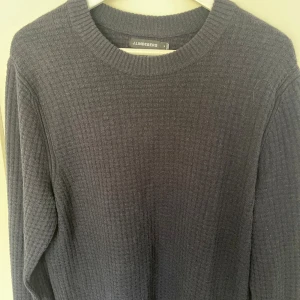 Mörkblå stickad tröja J.Lindeberg - Snygg mörkblå stickad tröja från J.Lindeberg i storlek M. Tröjan har ett strukturerat rutmönster, rund hals och ribbade muddar. Tillverkad i 100% bomull, perfekt för dig som gillar stilrena stickade tröjor. 