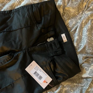 Svarta bootcut-byxor från Nelly - Snygga svarta bootcut-byxor från Nelly med glansig finish och markerade sömmar framtill. Byxorna har en låg midja, klassiska fickor och coola broderade detaljer på bakfickorna. Perfekt för dig som gillar trendiga och stilrena plagg(Helt oanvända och har lappen kvar)💓