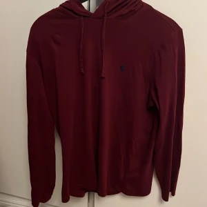 Ralph Lauren Hoodie - Säljer denna Ralph Lauren hoodie i väldigt fint skick. Det är en hoodie med tunt material och en snygg vinröd färg som passar perfekt till hösten. Hoodien är svår att hitta och är perfekt för en avslappnad lager på lager look.