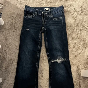 Mörkblå bootcut jeans med slitningar - Snygga mörkblå jeans med tydliga slitningar och hål på ena benet. Byxorna har kontrasterande vita sömmar och bootcut-modell och dem är från Gina. Jag har själv gjort hålet. Storlek är 158 men passar mig bra som har 164 och mer. 