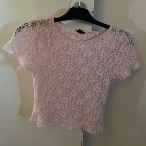 Ljusrosa spetsblus från Gina Tricot - Supersöt ljusrosa blus från Gina Tricot i spets med korta ärmar. Blusen har ett blommönster i spetsen och rund halsringning. Säljer toppen då jag använt den två gånger och den kommer inte till användning. 