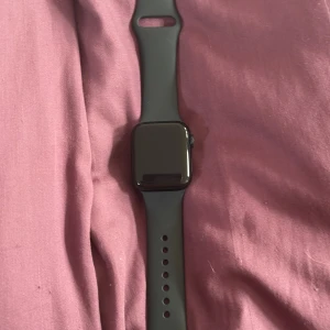 Apple Watch SE 40mm svart aluminium - Säljer en Apple Watch SE 40mm med svart aluminiumboett och svart silikonarmband. Klockan har en modern, fyrkantig design och passar perfekt för dig som gillar teknik och vill ha koll på allt direkt på handleden.