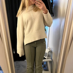 Beige stickad tröja från Zara  - Mysig beige stickad tröja med hög hals och breda ribbade muddar. Tröjan har en slits på båda sidorna av kanten precis vid höften och en dekorativ söm framtill. Tröjan är mjuk och härlig i storlek S