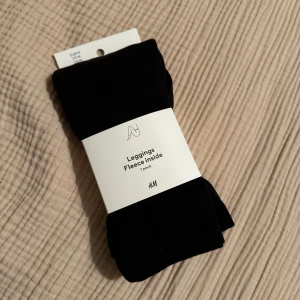Svarta fleecefodrade leggings H&M - Svarta leggings från H&M med mjuk fleece på insidan. Perfekta för kalla dagar när du vill ha både stil och värme. Stretchigt material som sitter skönt och följer kroppen.