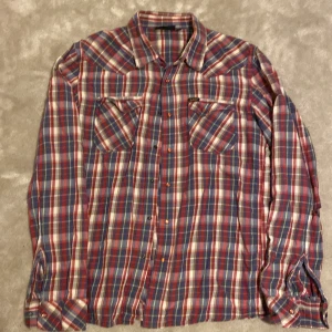 Rutig röd och blå skjorta från Lee - Rutig skjorta från Lee i storlek S. Skjortan har en  mix av rött, blått, vitt och lite gult, med två bröstfickor och  tryckknappar. Materialet är  bomull och modellen är långärmad med normal passform. Har ett hål på den vänstra armen. Är öppen för ett lägre pris vid snabb affär. Om ni har några frågor skriv gärna!