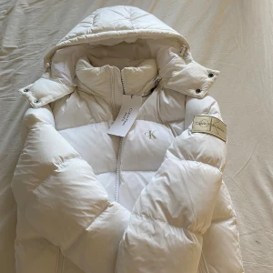 Vit pufferjacka från Calvin Klein Jeans - Snygg vit pufferjacka från Calvin Klein Jeans. Riktigt bra kvalite, den är otroligt varm och kommer få dig se clean ut denna vinter. Säljer för jag köpte i fel storlek och klippte bort en tagg som gjorde att den inte får skickas tillbaka. Den är i xs passar mig som har s men inte vid halsen när man stänger den. ANVÄND ENDAST 2 gånger OCH KOM IKTE MED EN PRISSÄKNING