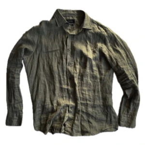 Olivgrön linneskjorta från Massimo Dutti - Olivgrön skjorta i 100% linne från Masimmo Dutti. Klassisk krage, knäppning framtill och långa ärmar med manschettknappar. Skjortan har en avslappnad passform och är perfekt för en stilren och chill look.