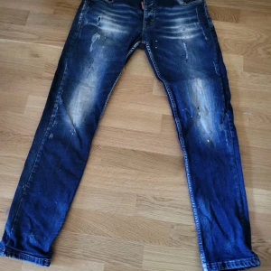 dsquared jeans herr - Säljer ett par blå jeans med coola slitningar och färgstänk framtill. Jeansen har raka ben, klassiska bakfickor och en unik patch bak i midjan. Materialet är jeans och de har en snygg tvättad look som ger en avslappnad vibe.