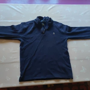 Marinblå fleece-tröja Polo Ralph Lauren - Mysig marinblå fleece-tröja från Polo Ralph Lauren i barn storlek XL vilket motsvarar xs .Tröjan har half zip-dragkedja, lång ärm och klassisk broderad logga på bröstet. Perfekt för kyliga dagar och enkel att matcha med jeans eller joggers.