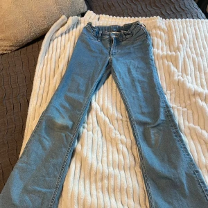 Blå flared jeans från H&M - Snygga blå jeans från H&M med flared ben och låg midja. Jeansen har justerbar midja och klassisk femficksdesign. Perfekt för dig som gillar retrovibbar och vill ha en cool siluett. Materialet är mjukt denim med lite stretch för extra komfort.