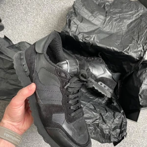 Valentino Garavani Rockrunner sneakers - Snygga svarta Valentino Garavani Rockrunner sneakers med coola camouflagedetaljer. Skorna har en mix av skinn, mocka och textil, samt ikoniska nitar på hälen. Perfekta för dig som vill ha en lyxig och edgy look till vardags. Klassisk snörning och bekväm platt sula.