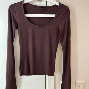 Brun långärmad topp från Gina Tricot - Säljer en enkel och stilren brun långärmad topp från Gina Tricot i storlek XS. Toppen har en rundad halsringning och är figurnära i passformen. Perfekt att matcha med jeans eller kjol för en clean look.