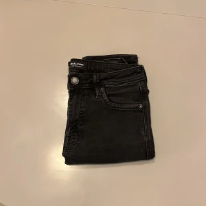 Svarta slim jeans Jack & Jones Glenn - Svarta jeans från Jack & Jones i modellen Glenn med slim fit. Klassisk femficksdesign, silverfärgade nitar och knapp. Jeansen är tillverkade i ett stretchigt bomullsmaterial för en bekväm passform. Storlek 27/30