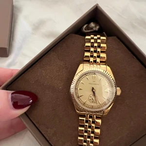 Mockberg Royal Watch 28 mm guld - Snygg Mockberg Royal Watch med 28 mm urtavla, aldrig använd då jag fått i present och för sent att skicka tillbaka. guld PVD-plätering och länkarmband i stål. Klockan har en rund urtavla med minimalistiska index och en liten sekundvisare. Kommer med original ask och tygpåse. Perfekt accessoar för dig som gillar stilrena detaljer. PRIS KAN DISKUTERAS