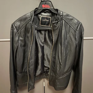 Svart skinnjacka från Soyaconcept - Snygg svart skinnjacka från Soyaconcept med quiltade detaljer på axlar och nederkant. Jackan har dragkedja framtill och en stilren, klassisk look som passar perfekt till jeans eller klänning. Materialet är mjukt och följsamt för en cool vibe.