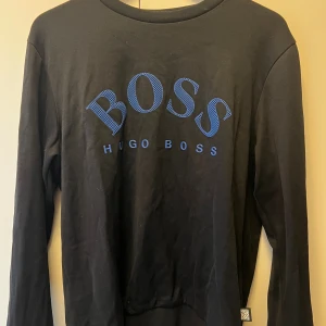 Svart långärmad tröja Hugo Boss - Svart långärmad tröja från Hugo Boss med blått tryck på bröstet. Tröjan är i storlek m. 