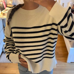 Randig stickad tröja - Säljer en snygg stickad tröja i vitt med svarta ränder. Tröjan har ribbade muddar, passformen är lite loose och den har små slitsar i sidorna. Skriv för fler bilder!
