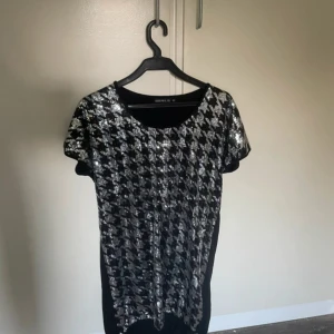 Svart och silver paljettklänning Girls - Kort svart klänning med glittriga silverpaljetter framtill i ett rutigt mönster. Rund halsringning och korta ärmar. Baksidan är helsvart och i mjukt tyg. Perfekt för dig som vill sticka ut med lite extra bling och coolt mönster. Stl är 170 men passar perfekt för xs och s. Perfekt till halloween, nyår, fest eller kanske bara en fin dag 