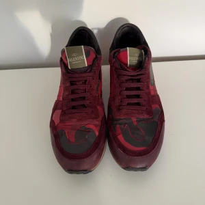 Valentino Rockrunner sneakers röd camo - ( har kvitto och box) Snygga Valentino Rockrunner sneakers i vinröd och svart camo-mönster. Skorna har detaljer i mocka och skinn, klassisk snörning och coola nitar på hälen. Perfekta för dig som vill sticka ut med exklusiva och trendiga sneakers.