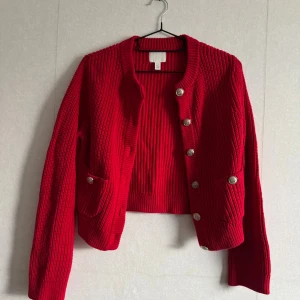Röd stickad kofta med silvriga knappar - Säljer en röd stickad kofta från H&M  med grov ribbad struktur och snygga silvriga knappar framtill. Storlek XXS men som motsvarar XS för mig. 