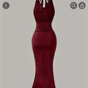 Vinröd långklänning med knyt i nacken - Supersnygg vinröd långklänning med figurnära passform och knyt i nacken. Klänningen har ärmlös design och markerad midja med lätt rynkade detaljer. Tillverkad i ett glansigt, stretchigt material som ger en lyxig känsla.