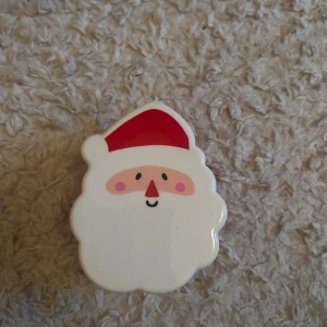 Julig plastburk med tomtemotiv - Söt liten plastburk i form av en tomte, perfekt för småsaker eller godis till jul. Burken är i gott skick utan synliga skador eller slitage. Locket är lätt att ta av och sätta på. Passar utmärkt som dekoration eller presentförpackning.