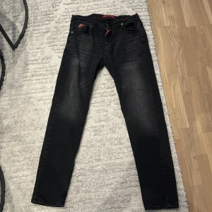 Svarta jeans från Dsquared2 - Snygga svarta jeans från Dsquared2 med diskret tvättad look och röda detaljer. Klassisk femficksmodell med DSQ-logga på bakfickan och liten röd etikett fram. Jeansen har smal passform och är tillverkade i mjukt denimtyg.
