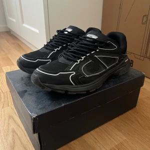 Svarta  B30 sneakers - Säljer ett par svarta B30 sneakers med coola silvriga detaljer och tydlig CD-logga på hälen. Skorna har snörning, rund tå och platt sula. Materialet är en mix av mesh och syntet, vilket ger en sportig vibe och skön komfort. Perfekta för dig som gillar exklusiva och trendiga sneakers.