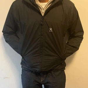 Svart vindjacka från Haglöfs, stl S - Svart vindjacka från Haglöfs med huva och dragkedja framtill. Jackan har justerbara ärmslut med kardborre och två sidofickor med dragkedja. Perfekt för blåsiga dagar och enkel att matcha med allt. Klassisk logga på bröstet.priset kan diskuteras lägg ett bud hjärna