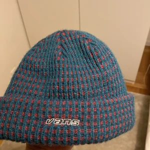 Blå och röd mössa från Vans - Mössa från Vans i blått med röda detaljer. Vans-loggan broderad framtill. Tillverkad i 100% akryl. Är öppen för ett lägre pris vid snabb affär. Om ni har några frågor skriv gärna!