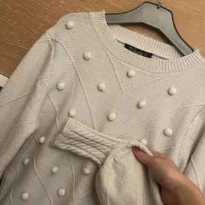 Vit stickad tröja med bollar Simplee - Superfin vit stickad tröja från Simplee med coola stickade bollar och diskret mönster framtill. Tröjan har rund hals, långa ärmar och ribbade muddar. Perfekt för dig som gillar mysiga och trendiga plagg med det lilla extra. Jättefin på!