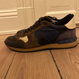 Valentino Garavani Rockrunner sneakers - Säljer ett par Valentino Garavani Rockrunner sneakers med camouflagemönster i grönt, blått, beige och svart. Skorna har snörning, platt sula och detaljer i mocka och skinn. Ikoniska nitar på hälen och rund tå. Dessa är i storlek 43 och kan sitta bra i 44. Skick 7,5/10