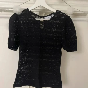 Svart spetsblus från Vila - Säljer en svart blus från Vila med korta puffärmar och rund hals. Blusen är helspetsad med snyggt mönster och har en liten öppning med knapp i nacken. Perfekt för dig som gillar detaljer och vill ha en feminin look.