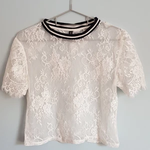 Vit spetsblus med sportig krage - Superfin vit blus i spets från H&M med blommigt mönster och korta ärmar. Sportig ribbad krage med svarta och vita ränder ger en cool kontrast. Perfekt att styla med jeans eller kjol för en trendig look.