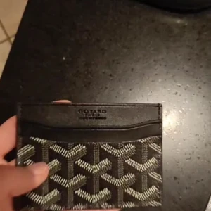 Svart plånbok med mönster - Snygg svart plånbok med grafiskt mönster i vitt och grått. Plånboken är tunn och smidig, perfekt för kort och sedlar. Tillverkad i skinn med flera kortfack och stilren design.