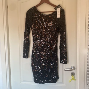 Svart paljettklänning från Nelly - Snygg svart kortklänning från NLY ONE med massor av glittriga paljetter. Klänningen har lång ärm och djup rygg, perfekt för att sticka ut. Materialet är polyester och den har en figurnära passform som framhäver siluetten.