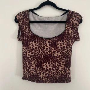 Leopardmönstrad topp från SHEIN XS - Säljer en kortärmad topp från SHEIN i storlek XS med leopardmönster. Toppen har en djup rundad urringning med svart spetskant. Den är ganska kort!!