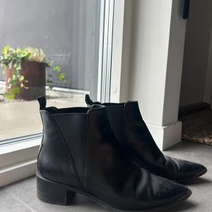 Svarta chelsea boots Acne Studios - Snygga svarta chelsea boots från Acne Studios i skinn med spetsig tå och låg klack. Klassisk och stilren modell med resår på sidorna och dragflik bak. Perfekta för dig som gillar minimalistisk och trendig stil.