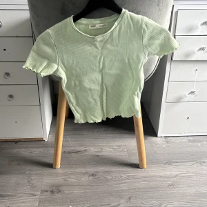 Ljusgrön ribbad croppad topp - Säljer en ljusgrön croppad topp från Pull&Bear med ribbad struktur. Toppen har korta ärmar och vågig kant nertill och vid ärmslut. Perfekt för dig som gillar en enkel men trendig stil.