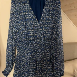 Blåmönstrad långärmad klänning Zara - Supersnygg blå och vit mönstrad klänning från Zara med v-ringning och långa ärmar. Klänningen har ett abstrakt mönster, smock i midjan och lätt rynkade ärmslut. Perfekt för dig som gillar färg och mönster!