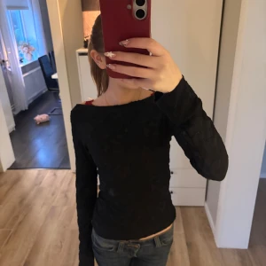 Svart blommig topp Gina Tricot  - Svart långärmad topp från Gina Tricot i storlek XS. Toppen har ett diskret blommönster i tyget och en tight passform med rundad halsringning. Perfekt att styla med jeans eller kjol för en snygg look.