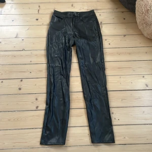 Svarta skinnbyxor från BikBok - Snygga svarta byxor i skinnimitation från BikBok, raka ben och klassisk femficksmodell. Byxorna har knapp och dragkedja framtill samt hällor för bälte. Perfekt för dig som vill ha en cool och trendig look.