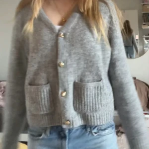 Grå kofta med guldknappar och fickor - Supermysig grå kofta från H&M med snygga guldknappar och två ribbade fickor framtill. Koftan har v-ringning och är stickad i mjukt material, perfekt för lager på lager. Jag har storlek XS/S och skulle säga att även om den är köpt i L så sitter den som en XS.