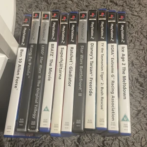 PlayStation 2 Spelpaket (12 titlar) - Samling med 12 PlayStation 2-spel, inklusive favoriter som Ratchet: Gladiator, LEGO Star Wars II, Star Wars Battlefront II, Ice Age 2 och fler. Alla spel med fodral, flera Platinum-utgåvor. Skick: bra, vissa fodral har mindre bruksspår. Perfekt för samlare eller familjer.