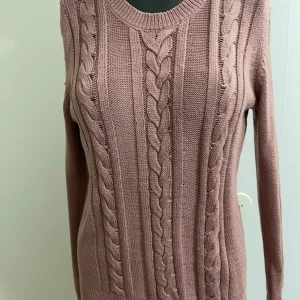 Stickad rosa tröja från Lindex - Supersnygg stickad tröja från Lindex i en dämpad rosa nyans. Tröjan har flätstickat mönster framtill, rund halsringning och långa ärmar. Perfekt för lager-på-lager och chill höst- eller vinterstil.