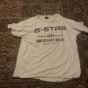 Vit G-Star t-shirt med tryck XL - Vit t-shirt från G-Star i storlek XL med svart tryck framtill där det står 'G-STAR RAW DENIM 3301 SOUTH EAST DISTR.'. Tillverkad i 100% bomull och har klassisk passform med korta ärmar och rund hals.